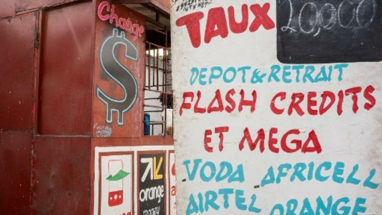 Signs advertise currency dealing and cellular phone charging on a cabin at a market in Kinshasa on August 11, 2021. – How to make the Congolese franc a strong enough currency to regain its rights against the omnipotent US dollar. The « de-dollarisation » of the economy, a sea serpent of Congolese financial policy, has just been put back on the drawing board in Kinshasa. The US dollar made its home in the former Zaire during the four-figure hyperinflation of the Mobutu years, as it did in other countries in the grip of chaos in Africa and elsewhere. (Photo by Arsene MPIANA / AFP)