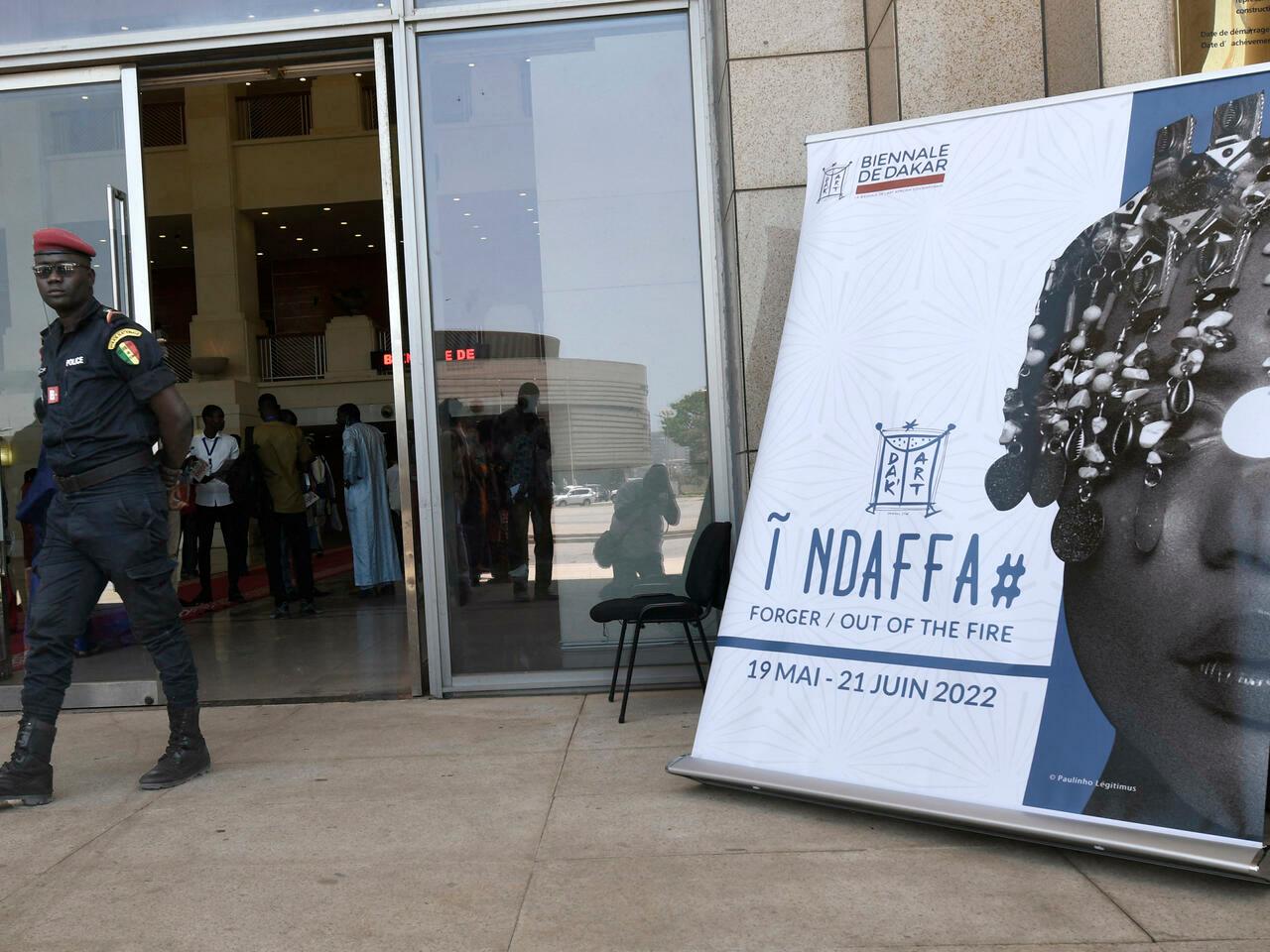 A Senegalese policeman walks past the offical poster of the 14th edition of the Biennale of Contemporary African art, May 19, 2022, at the great theater Doudou Ndaye Coumba Rose. – The 14th edition of the Biennale of Contemporary African Art, which has become the most important cultural event on the continent, opened Thursday in Dakar in the presence of Senegalese President Macky Sall, who presented the Grand Prix Léopold Sédar Senghor to an Ethiopian artist. (Photo by SEYLLOU / AFP)