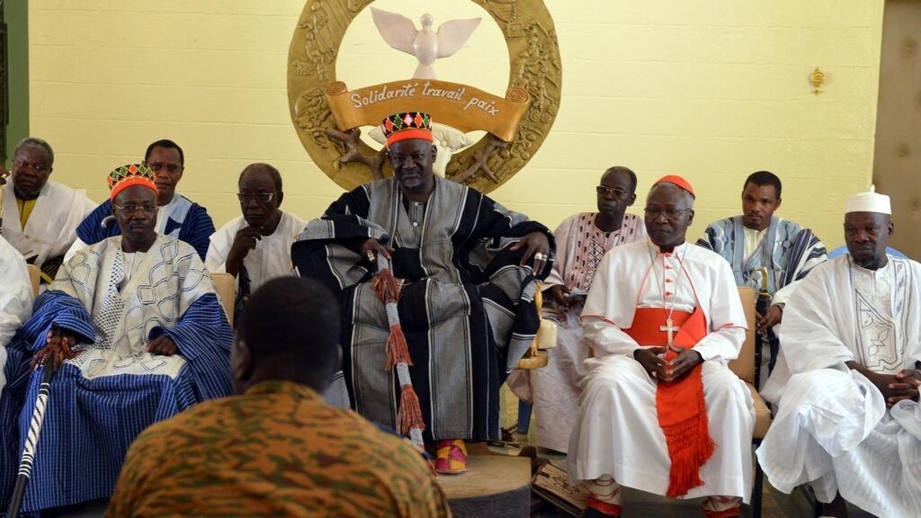 the Mogho Naba (C), the « king » of Burkina Faso&rsquo;s leading Mossi tribe, meets on November 4, 2014 with Burkina Faso&rsquo;s army-appointed leader, Lieutenant Colonel Isaac Zida (C, back), in Ouagadougou. Burkina Faso&rsquo;s army promised on November 4 to return power to a civilian government, an influential traditional chief said as the poor west African nation faced intense international pressure for a speedy transition following a military takeover. The meeting was one Zida and other military officers were holding with local leaders and envoys from abroad following the army&rsquo;s power grab on November 1 after a popular uprising toppled President Blaise Compaore on October 31. AFP PHOTO / ISSOUF SANOGO