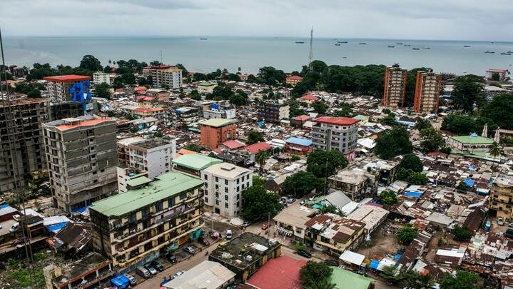 Shipping vessels sit on the waterway beyond commercial and residential buildings on the city skyline in Conakry, Guinea, on Saturday, Sept. 5, 2015. While Guinea produces bauxite, which is refined into aluminum, and has vast iron-ore deposits, its mining potential has been largely untapped because of political instability and a lack of infrastructure. Photographer: Waldo Swiegers/Bloomberg via Getty Images